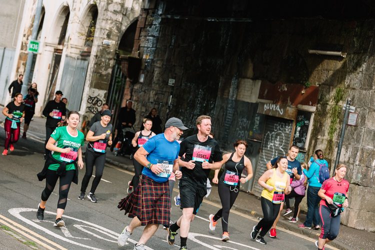 A group of Scots, one wearing a kilt, run under City Union Railway Bridge near Glasgow Green