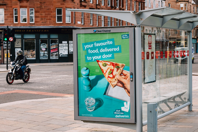Deliveroo app advert on the side of a bus stop outside Glasgow Green